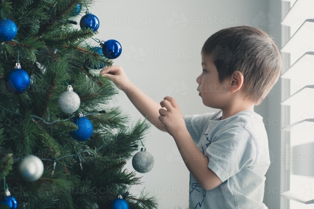 Cute mixed race boy hanging decorations on Christmas tree - Australian Stock Image