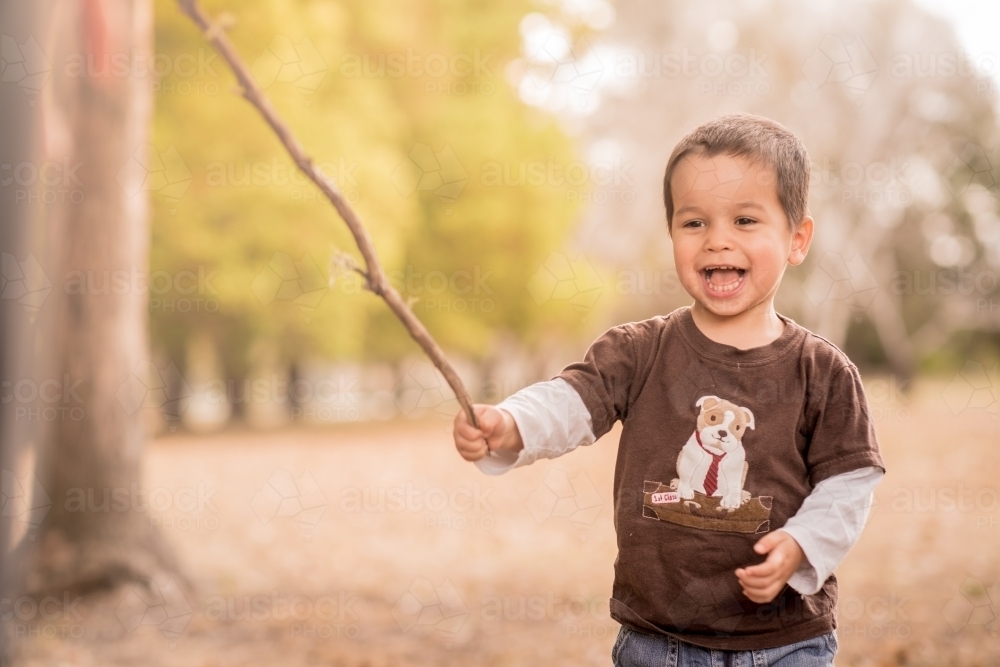 Cute mixed race boy playing in a park outside among the trees - Australian Stock Image