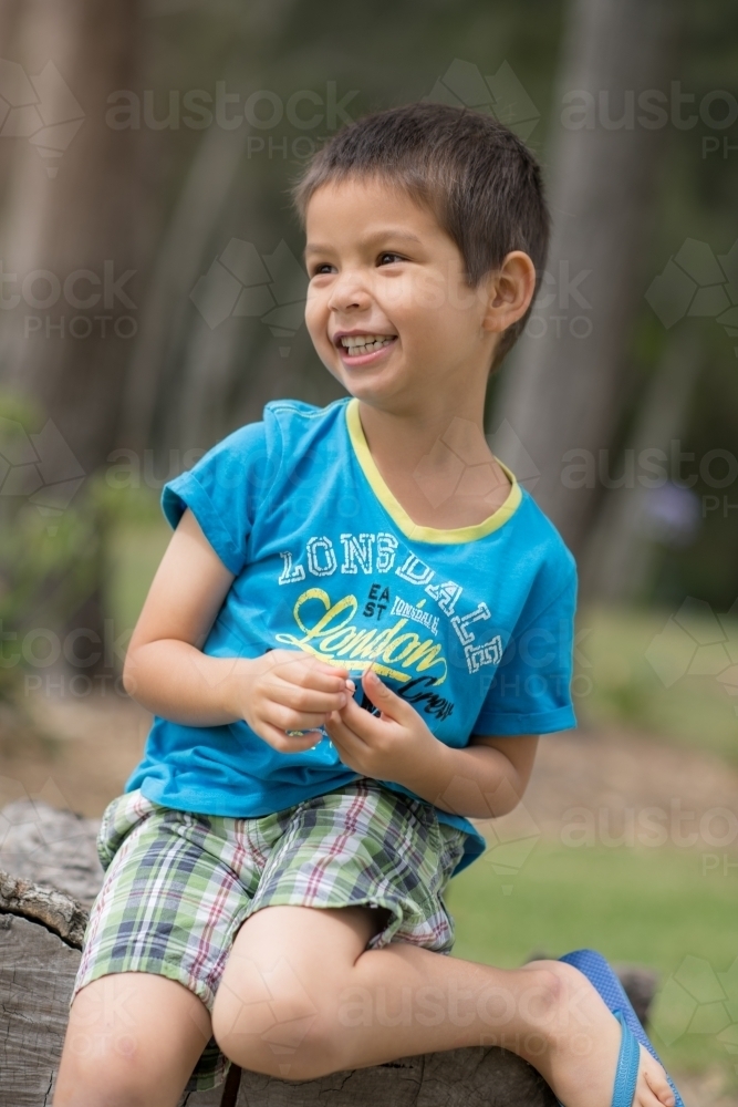 Cute mixed race boy playing in a park outside among the trees - Australian Stock Image