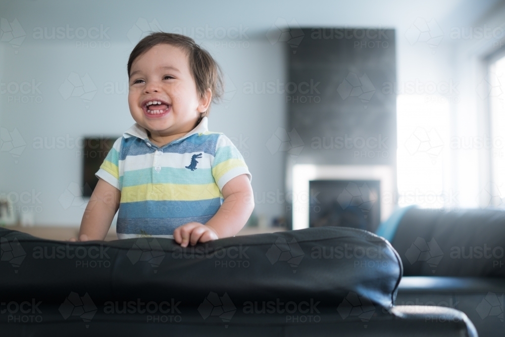 Cute mixed race toddler plays on a black leather lounge at home - Australian Stock Image