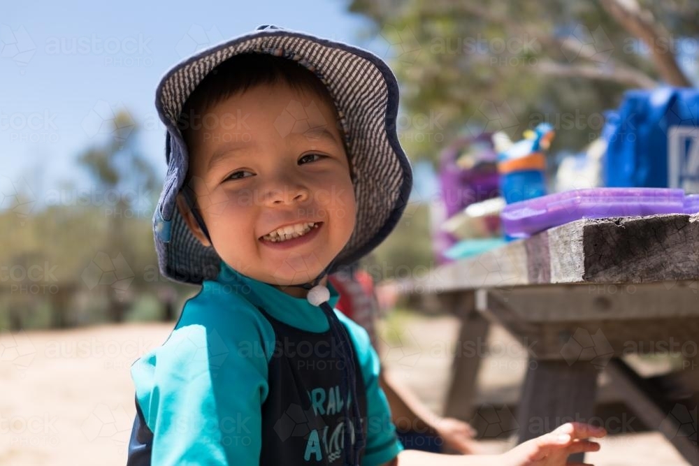 Cute two year old boy wearing a hat having a family picnic in the sun - Australian Stock Image