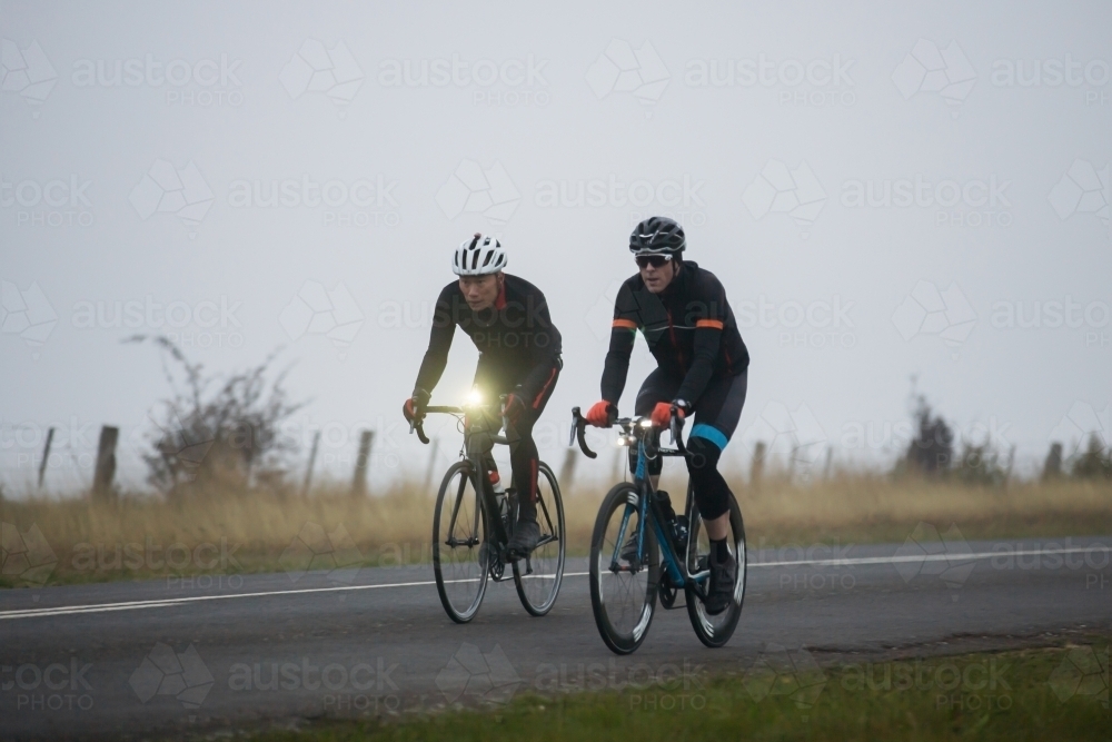 Cyclists riding in a foggy morning on a country road - Australian Stock Image