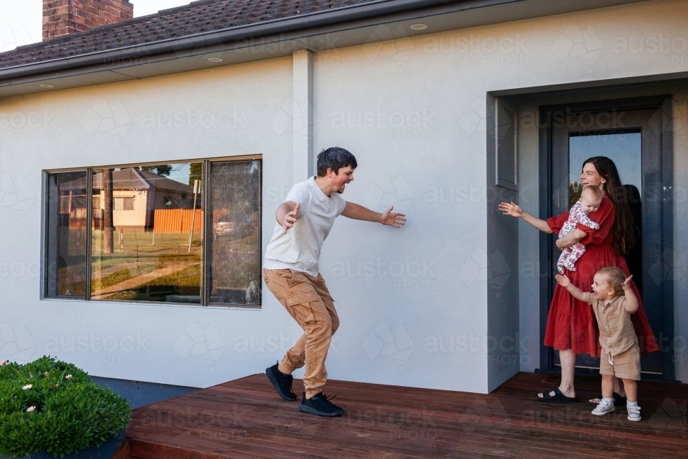 Dad getting home to family running to hug wife and children - Australian Stock Image