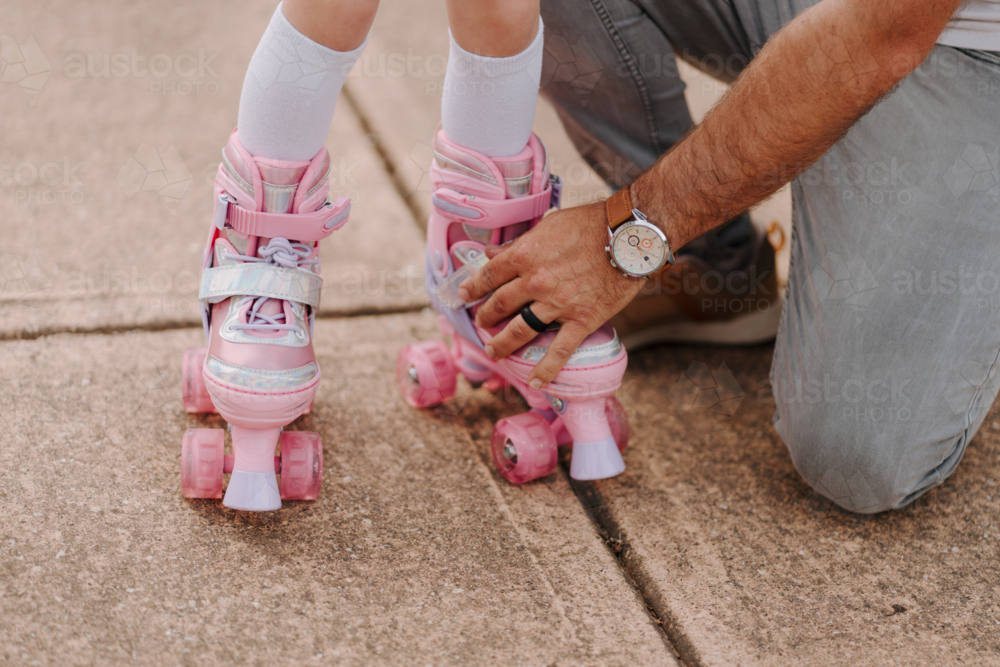 Dad helping daughter get into her roller blades. - Australian Stock Image