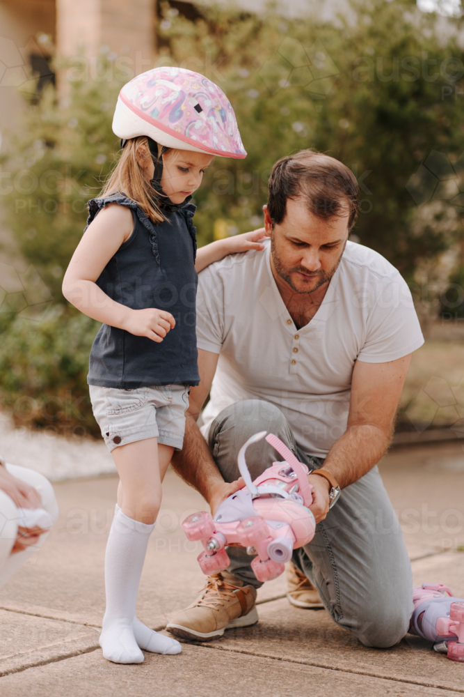 Dad helping daughter get into her roller skate gear. - Australian Stock Image