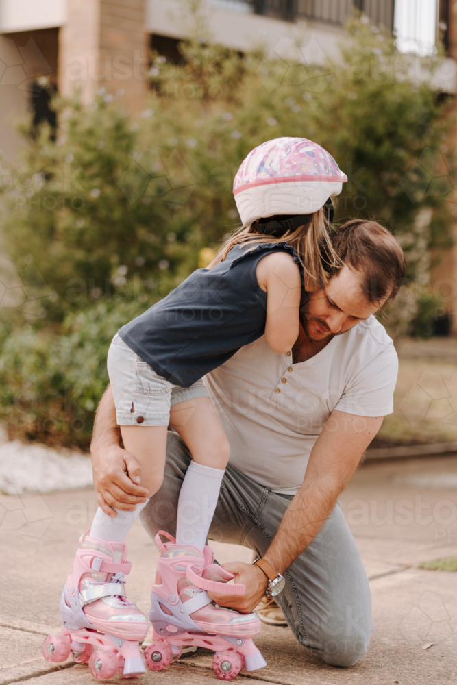 Dad helping daughter get into her roller skate gear. - Australian Stock Image