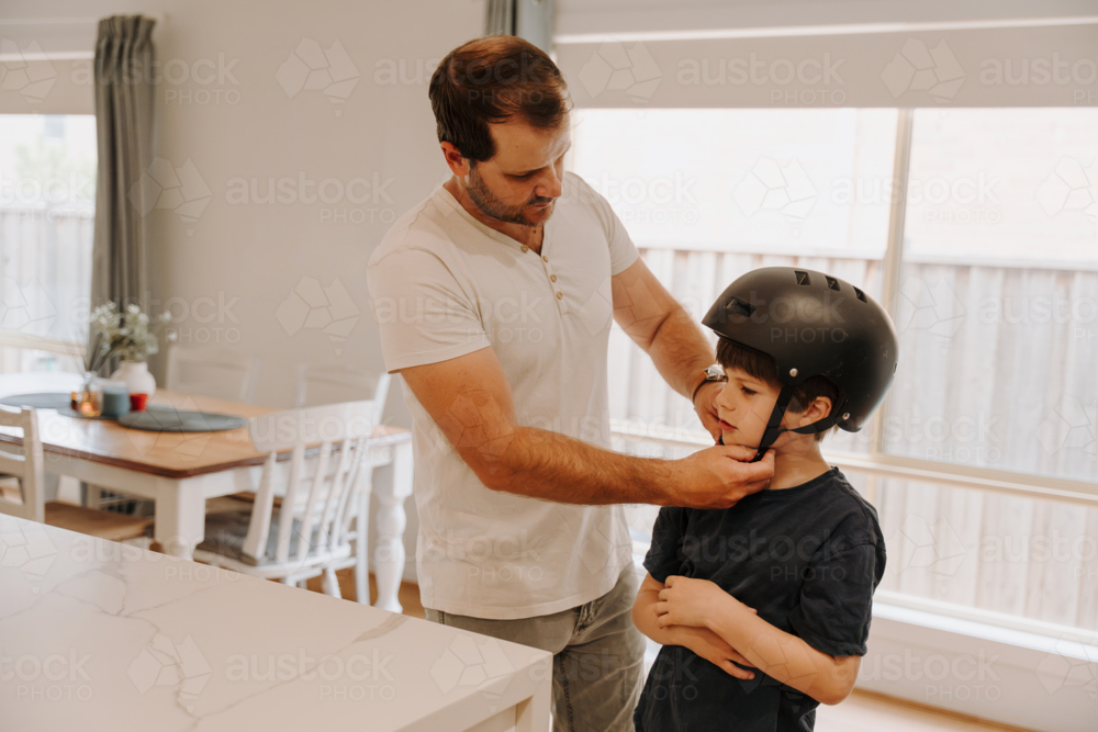 Dad helping his son put on his helmet. - Australian Stock Image