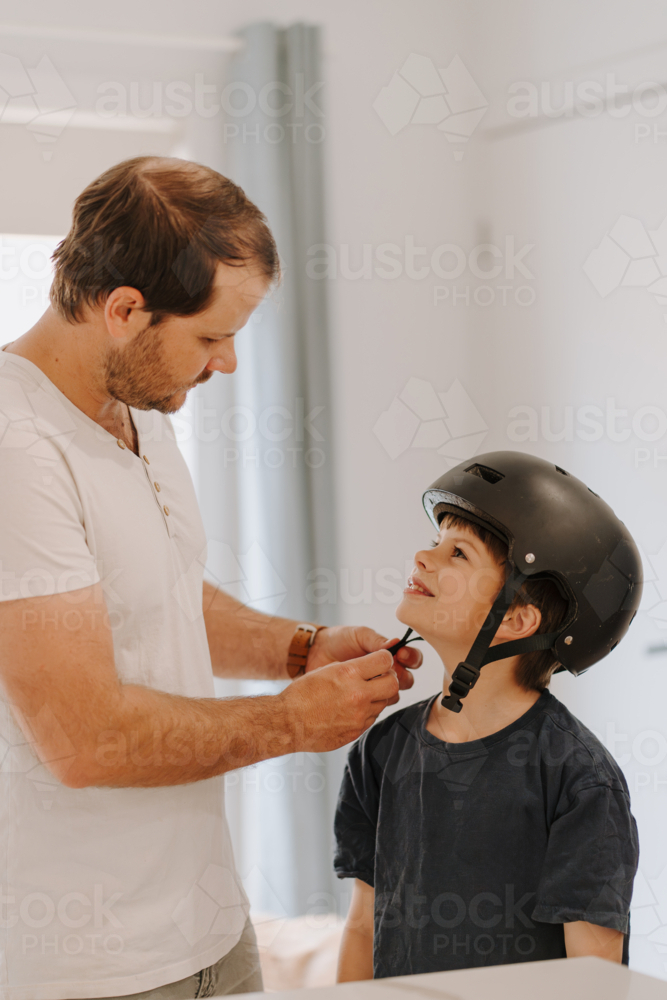 Dad helping his son put on his helmet. - Australian Stock Image