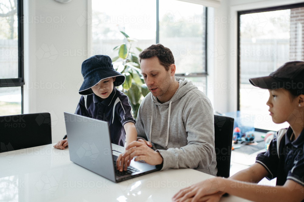 Dad helping kids with their homework using laptop. - Australian Stock Image