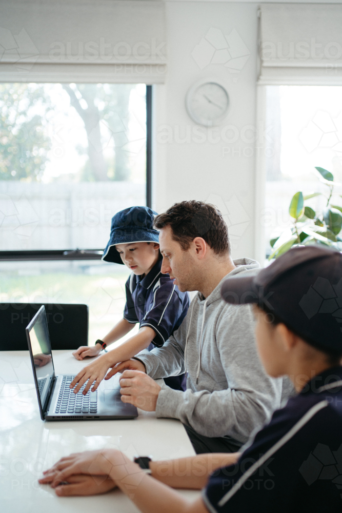 Dad helping kids with their homework using laptop. - Australian Stock Image