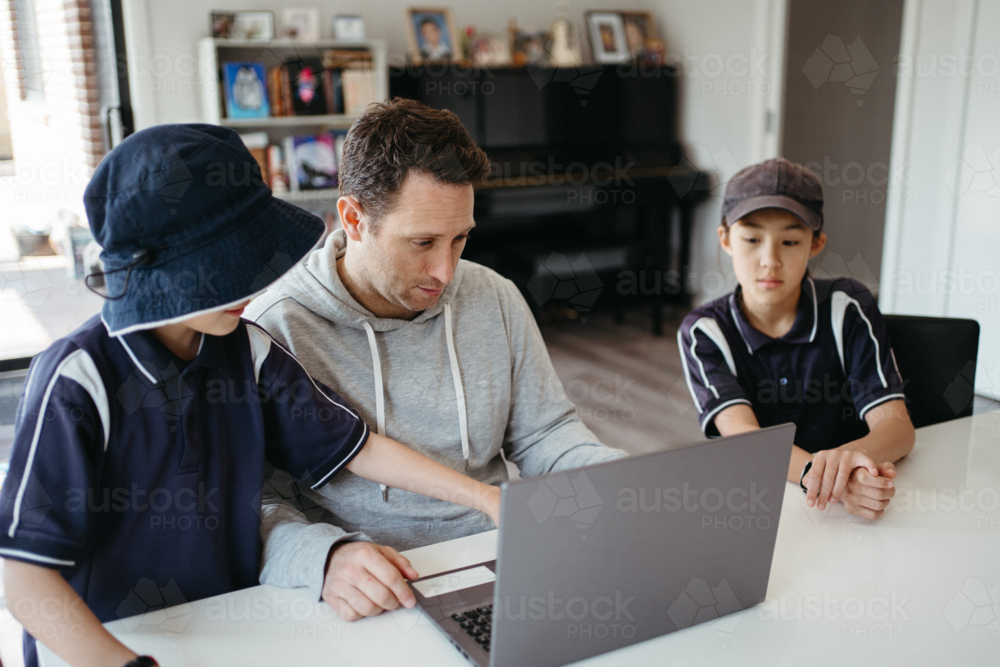 Dad helping kids with their homework using laptop. - Australian Stock Image