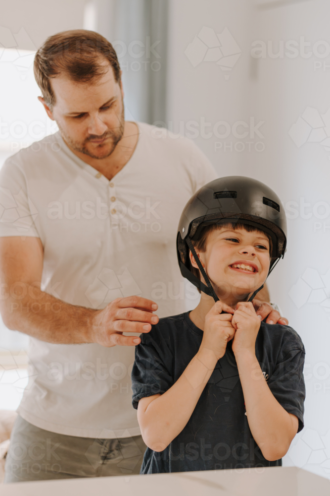 Dad helping son put on his helmet. - Australian Stock Image
