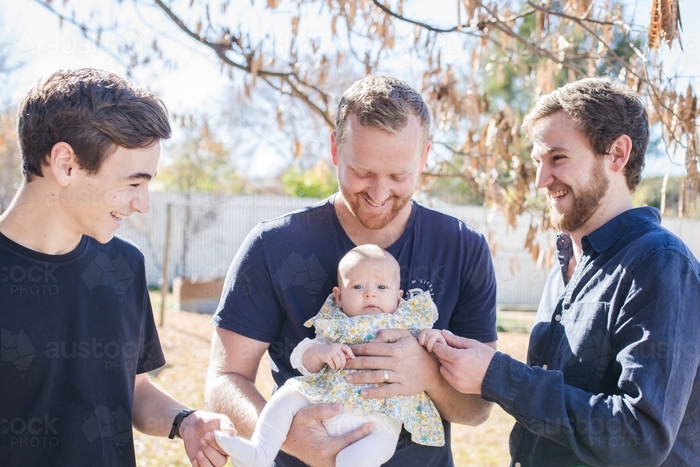 Dad holding baby girl with two brothers laughing - Australian Stock Image