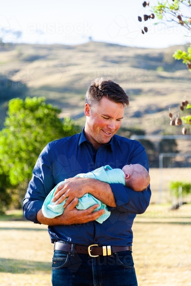 Dad holding his newborn baby daughter bonding and smiling - Australian Stock Image