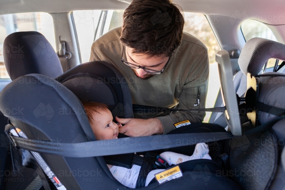 Dad putting baby into rear facing child car seat - clicked in safely - Australian Stock Image