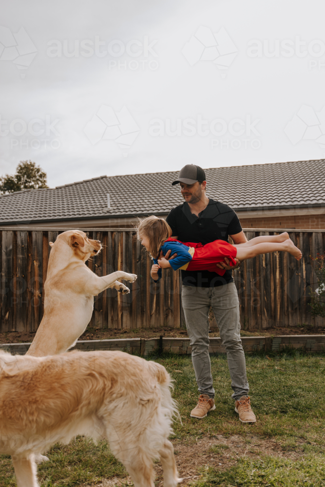 Dad simulating a flight for daughter in superhero costume. - Australian Stock Image