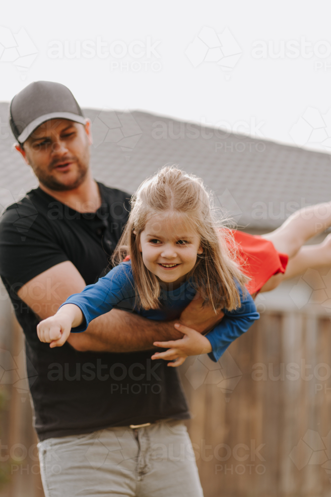 Dad simulating a flight for daughter in superhero costume. - Australian Stock Image