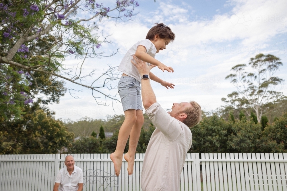 Dad throwing son upwards in backyard - Australian Stock Image