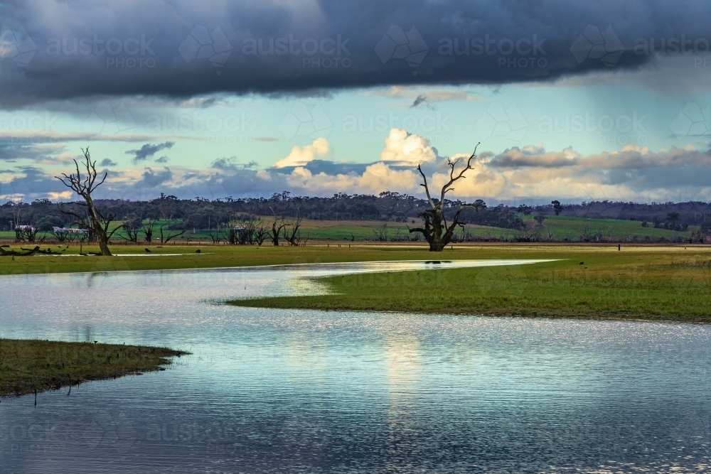 Dark cloud hovering over a winding river with thunder clouds in the distance - Australian Stock Image