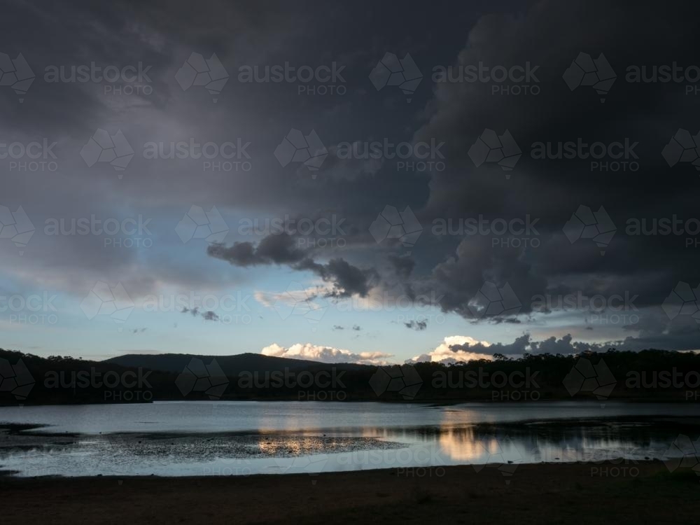 Dark storm clouds over a lake with reflections - Australian Stock Image