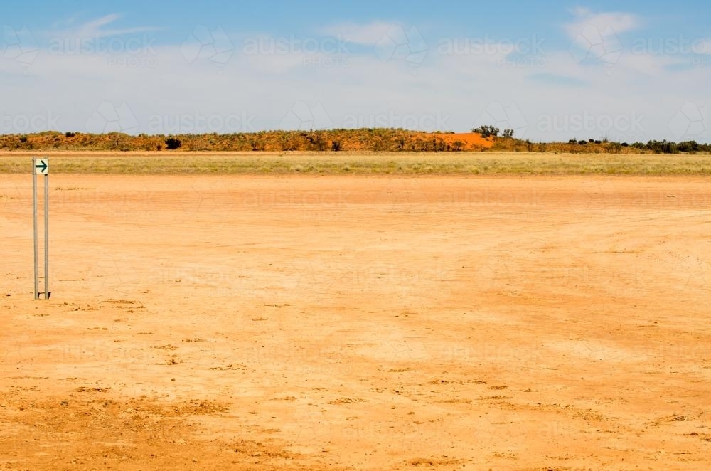 Direction arrow on a desert claypan with red sand dunes in the distance - Australian Stock Image