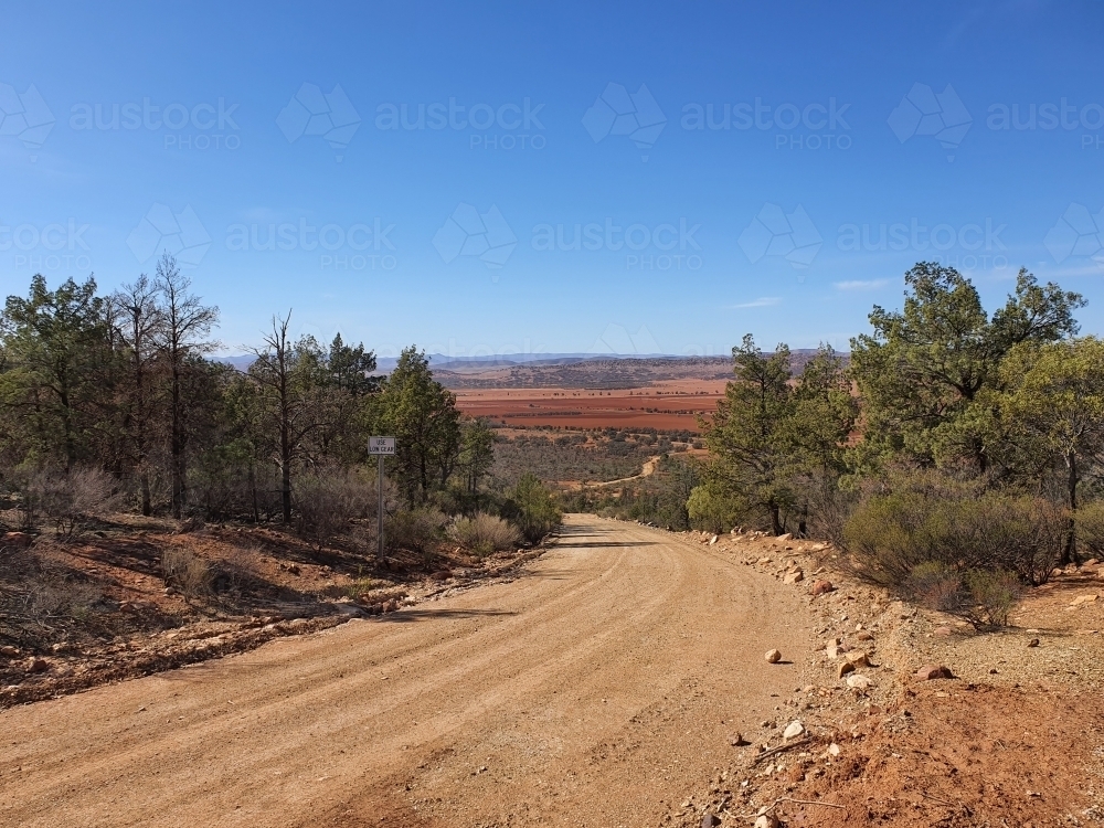 dirt road leading down hill to brown plains - Australian Stock Image