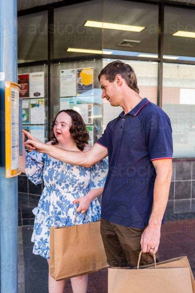 Disability worker NDIS provider helping young woman check bus time tables to catch public transport - Australian Stock Image