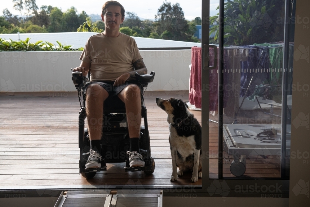 disabled man in wheelchair at home, with his dog sitting by - Australian Stock Image