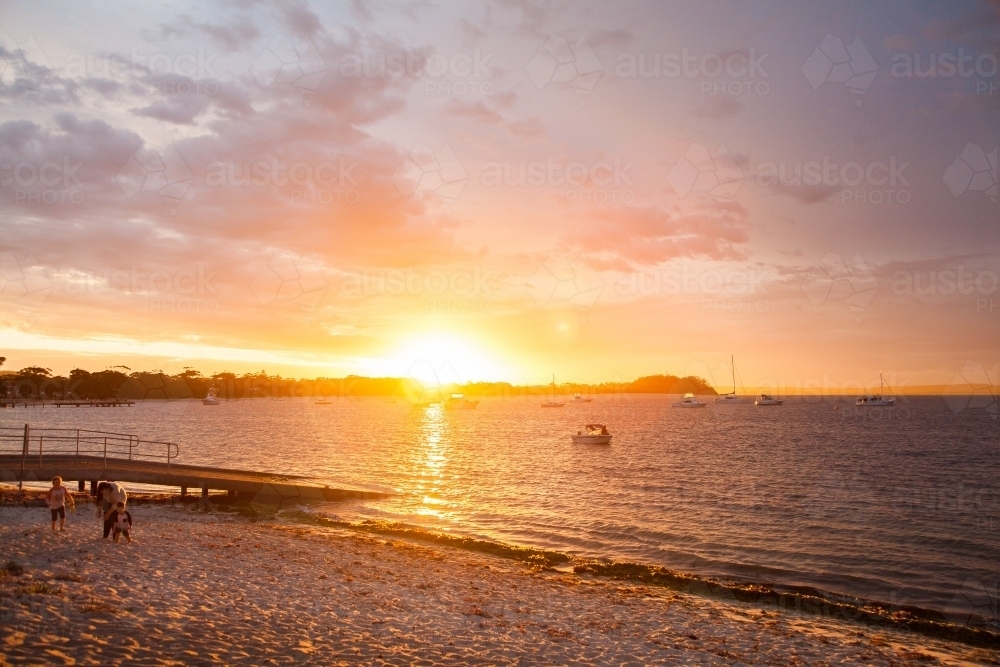 Distant family walking on a beach at sunset - Australian Stock Image