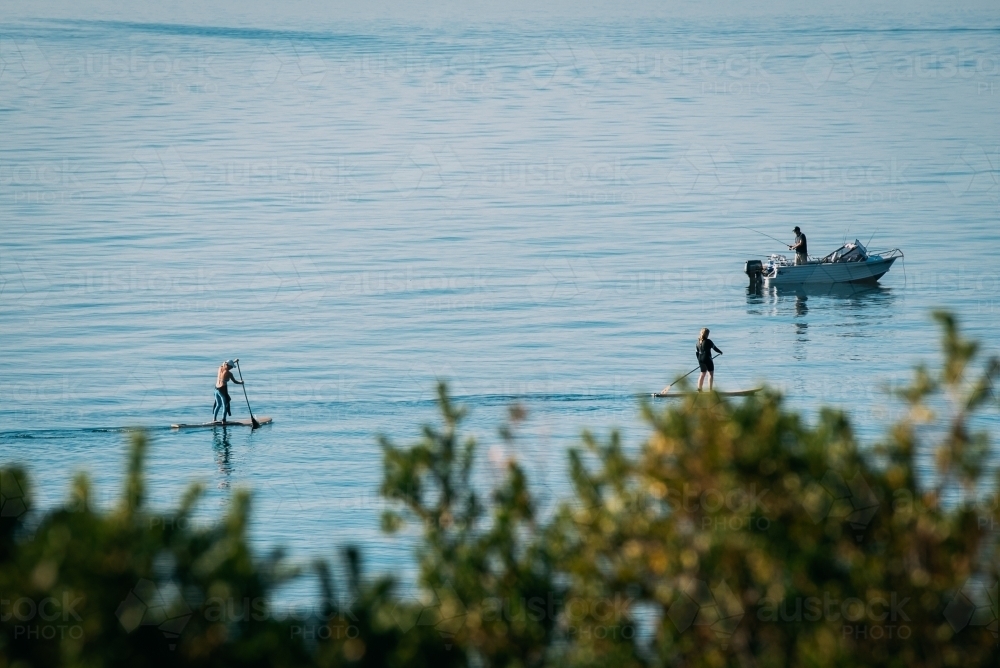 Distant people paddle boarding and fishing - Australian Stock Image