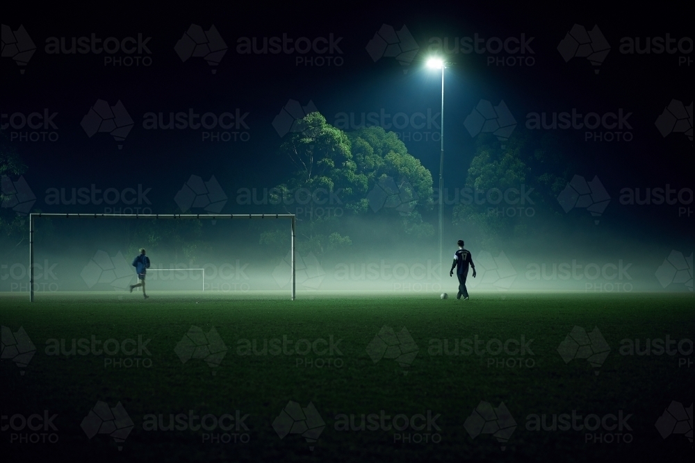 Distant people playing sport in fog at night - Australian Stock Image