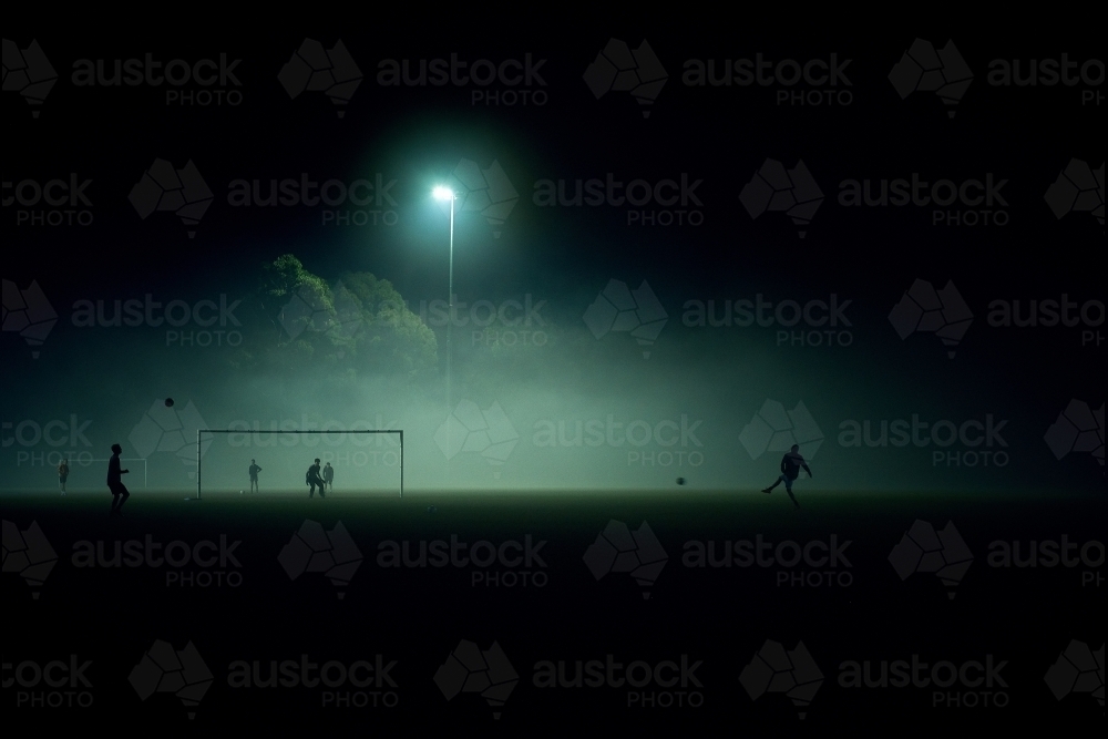 Distant people playing sports in fog at night - Australian Stock Image