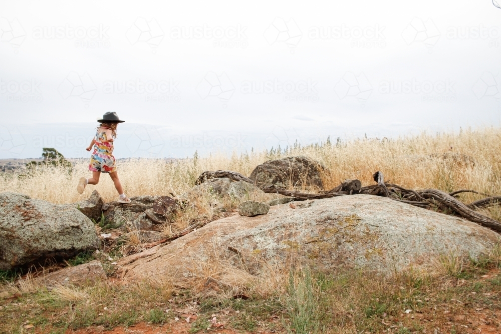 Distant shot of a young girl playing on rocky outcrop in grassy field - Australian Stock Image