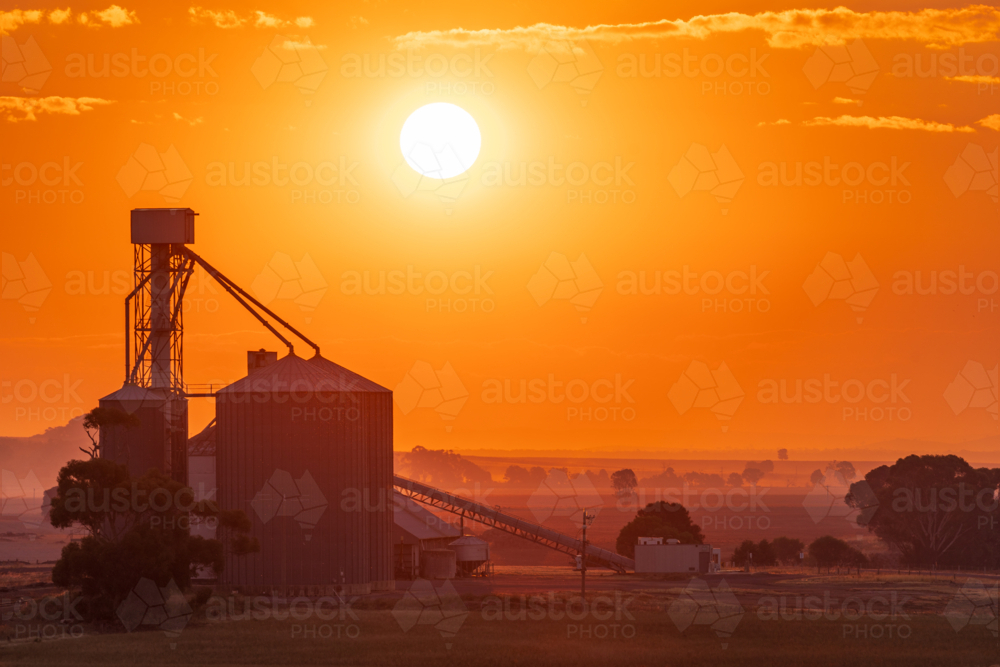 Distant view of a glowing sun in a golden sky over a grain silo - Australian Stock Image