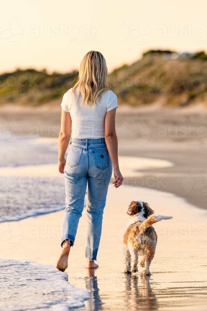 Dog and woman walking on the beach at sunset - Australian Stock Image