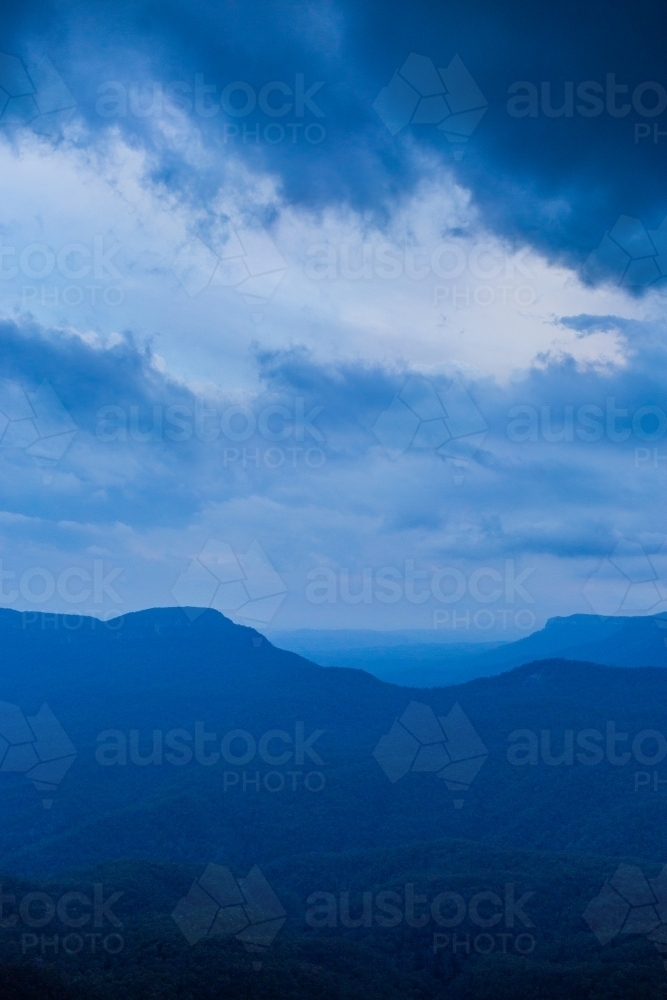 Dramatic stormy sky over layered blue mountains at nightfall - Australian Stock Image