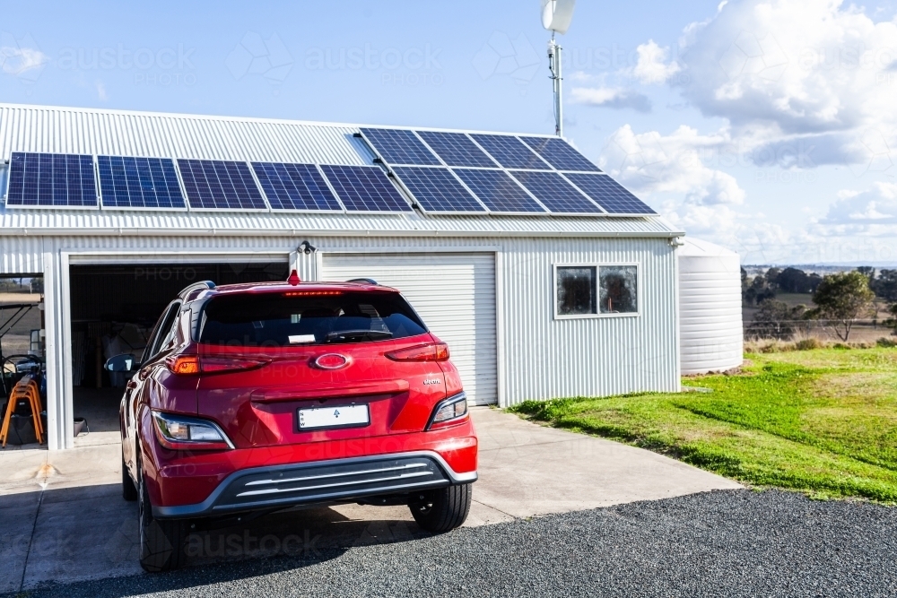 Driving electric vehicle car into solar and wind powered shed on country farm  - living sustainably - Australian Stock Image