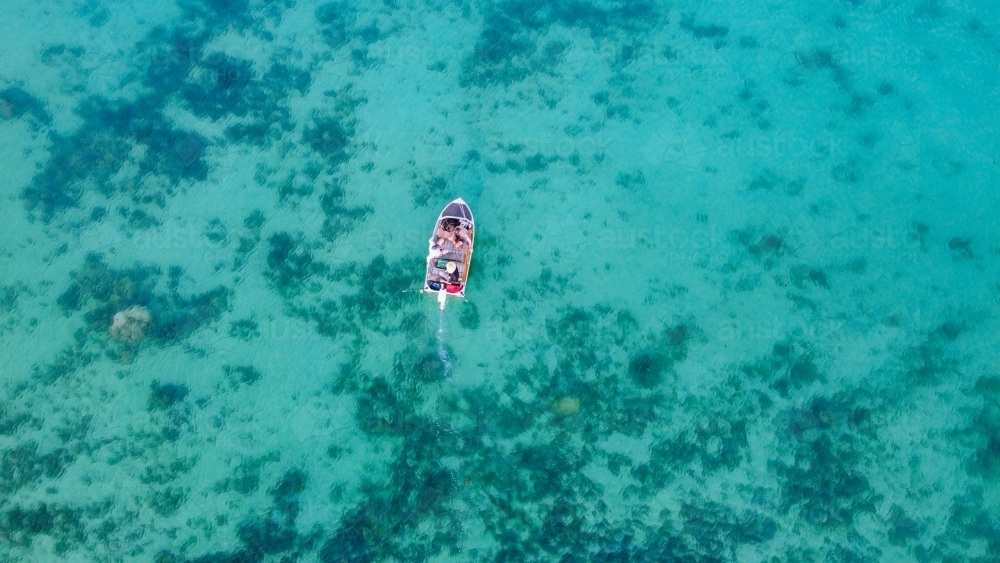 Drone shot of small tinny with people driving through turquoise waters with sand and coral below - Australian Stock Image