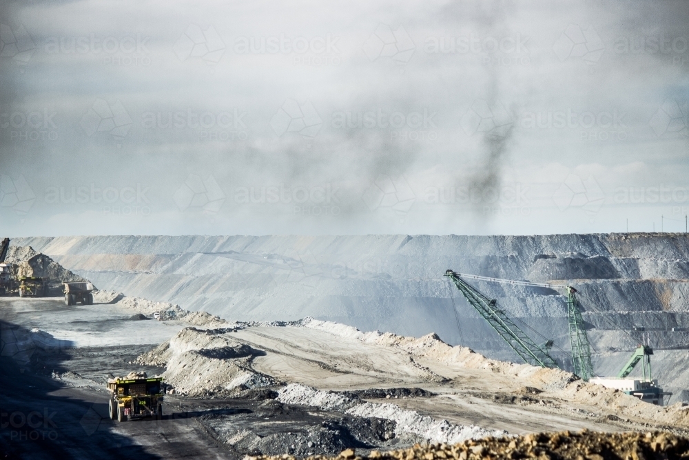 Dump trucks filling up with overburden and dragline in dusty open cut coal mine - Australian Stock Image