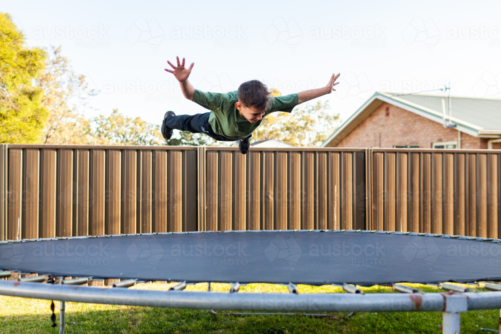 Eight year old Aussie kid jumping and playing on trampoline in backyard of suburban home - Australian Stock Image