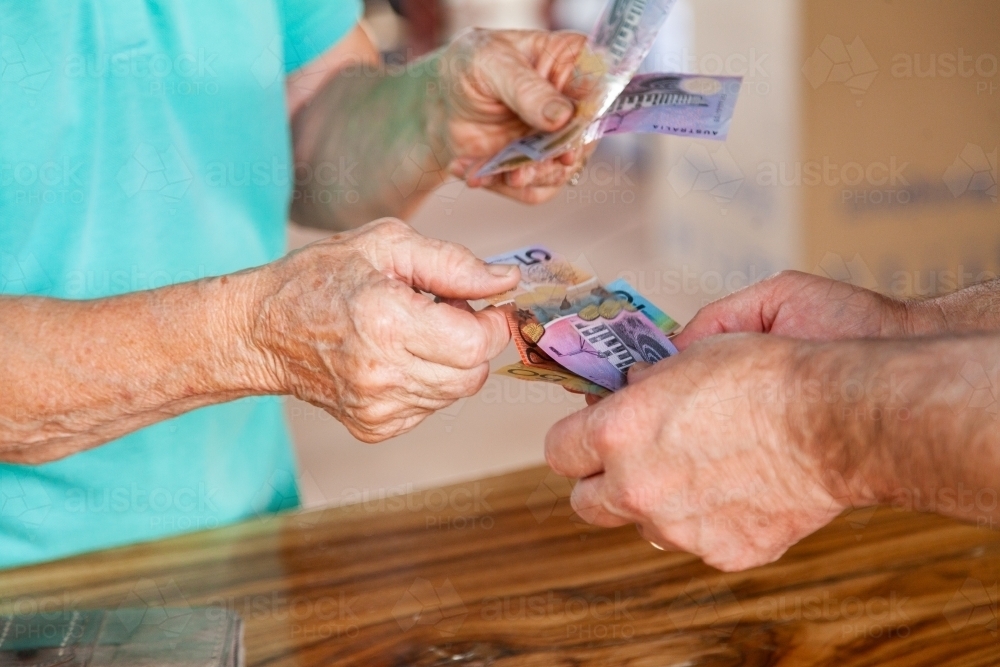 Elderly hands paying bill in cash - Australian Stock Image