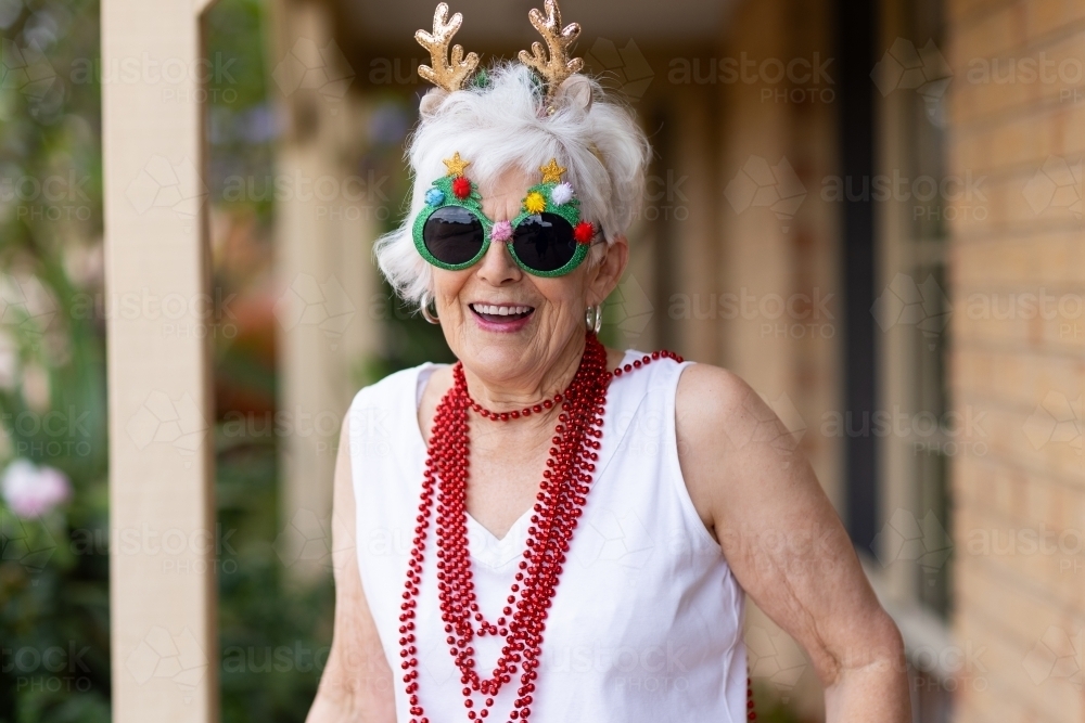 elderly lady having fun dressed up with glitter glasses for christmas - Australian Stock Image