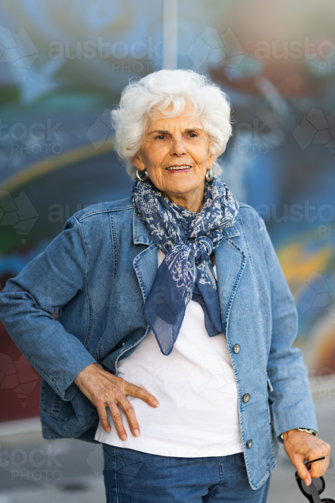 elderly lady wearing denim standing with hand on hip in blue toned image - Australian Stock Image