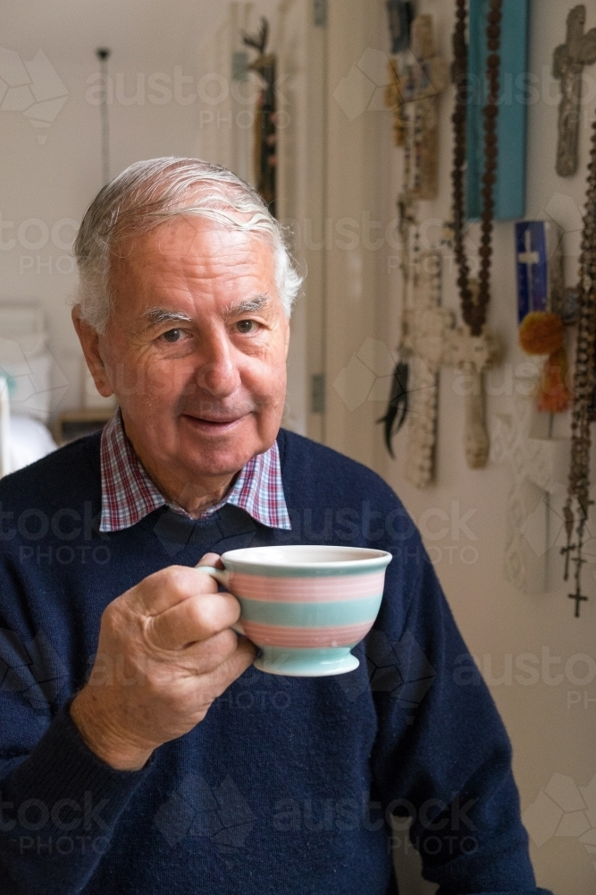 Elderly man holding a striped cup of tea - Australian Stock Image