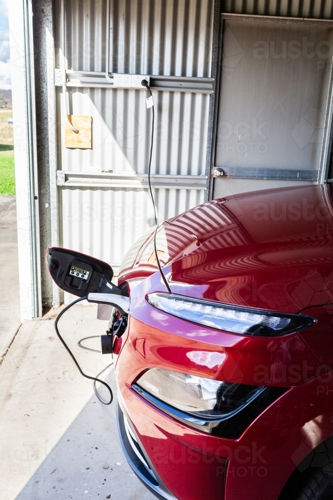 Electric vehicle car plugged in to charger in shed garage - Australian Stock Image