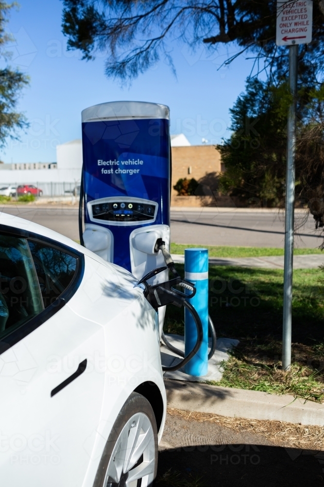 Electric vehicle fast charger with EV car plugged in to charge up on road trip - Australian Stock Image