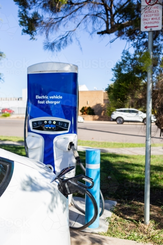 Electric vehicle fast charger with EV car plugged in to charge up on road trip - Australian Stock Image