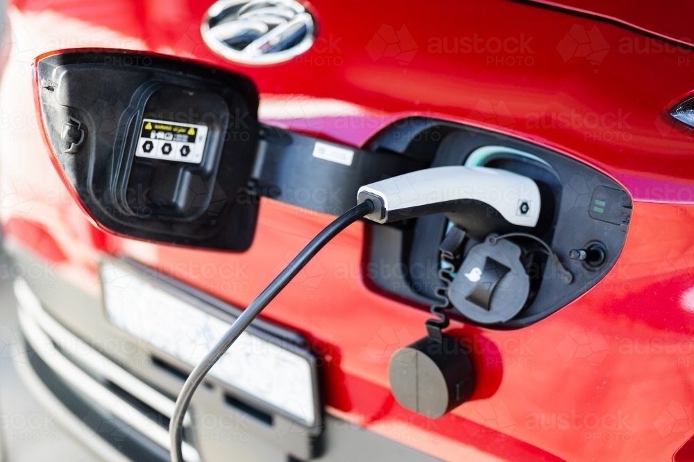 electric vehicle with home charging cable plugged in to front of red car - Australian Stock Image