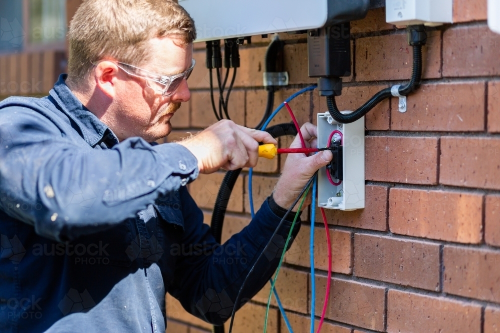 Electrician screwing in switch and electronics for solar power installation - Australian Stock Image