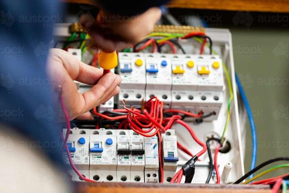 Electrician tradesman rewiring switch board for solar power - Australian Stock Image